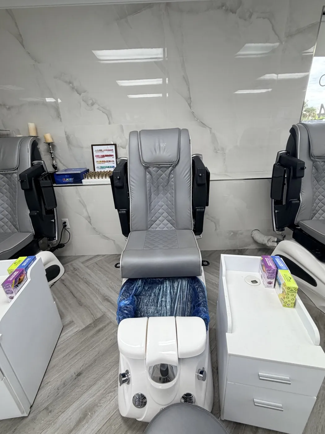 Gray leather pedicure chairs with white basins against a white marble wall