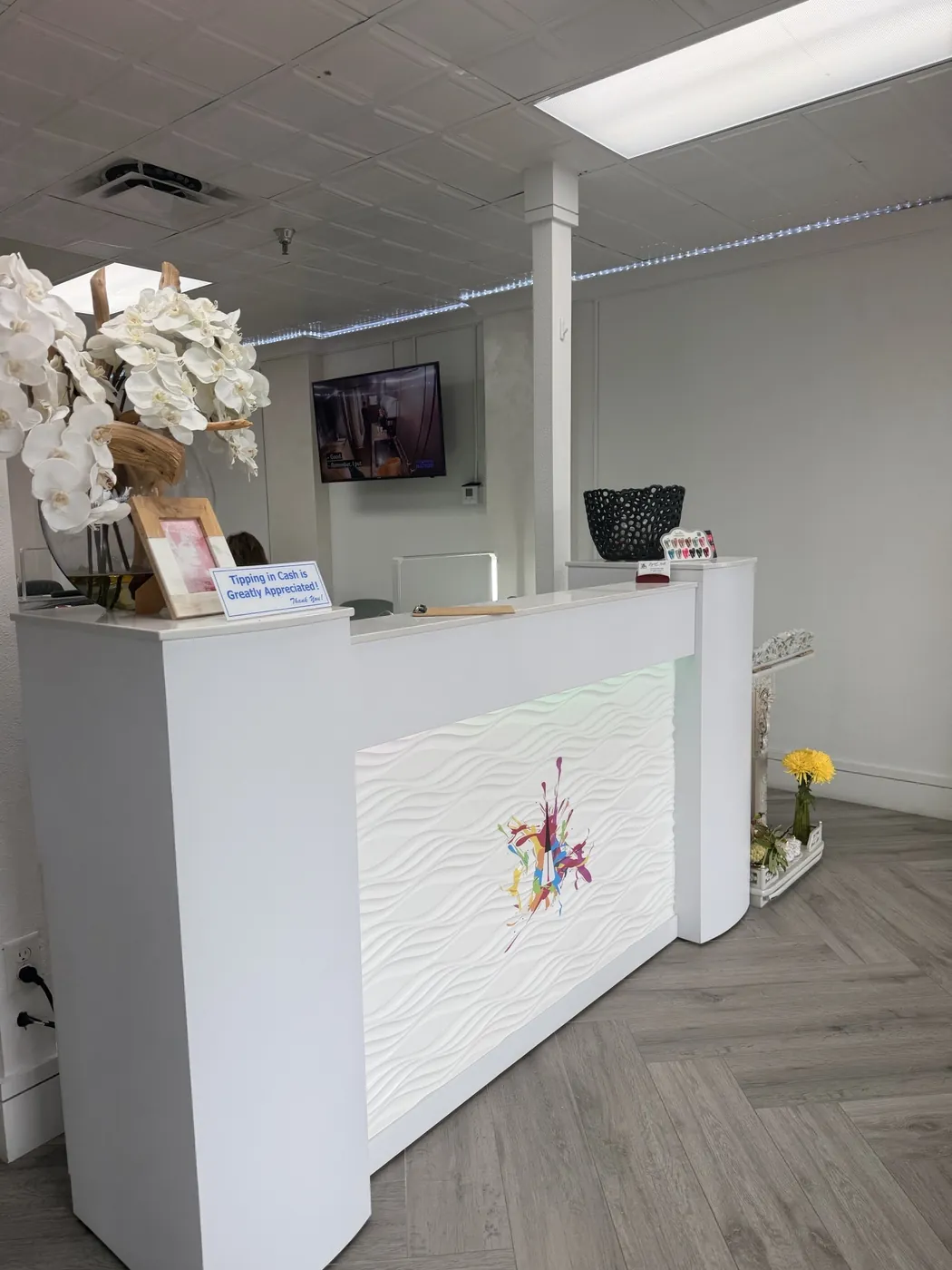 The white reception desk at Legend Nail Studio, with an orchid arrangement and the salon's logo on the front panel